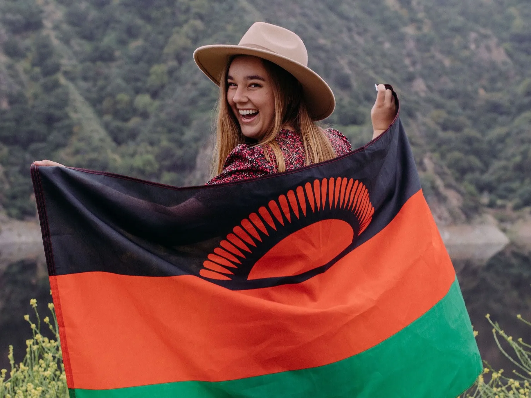 Ady holds the Malawian flag behind her and looks back with a big smile.