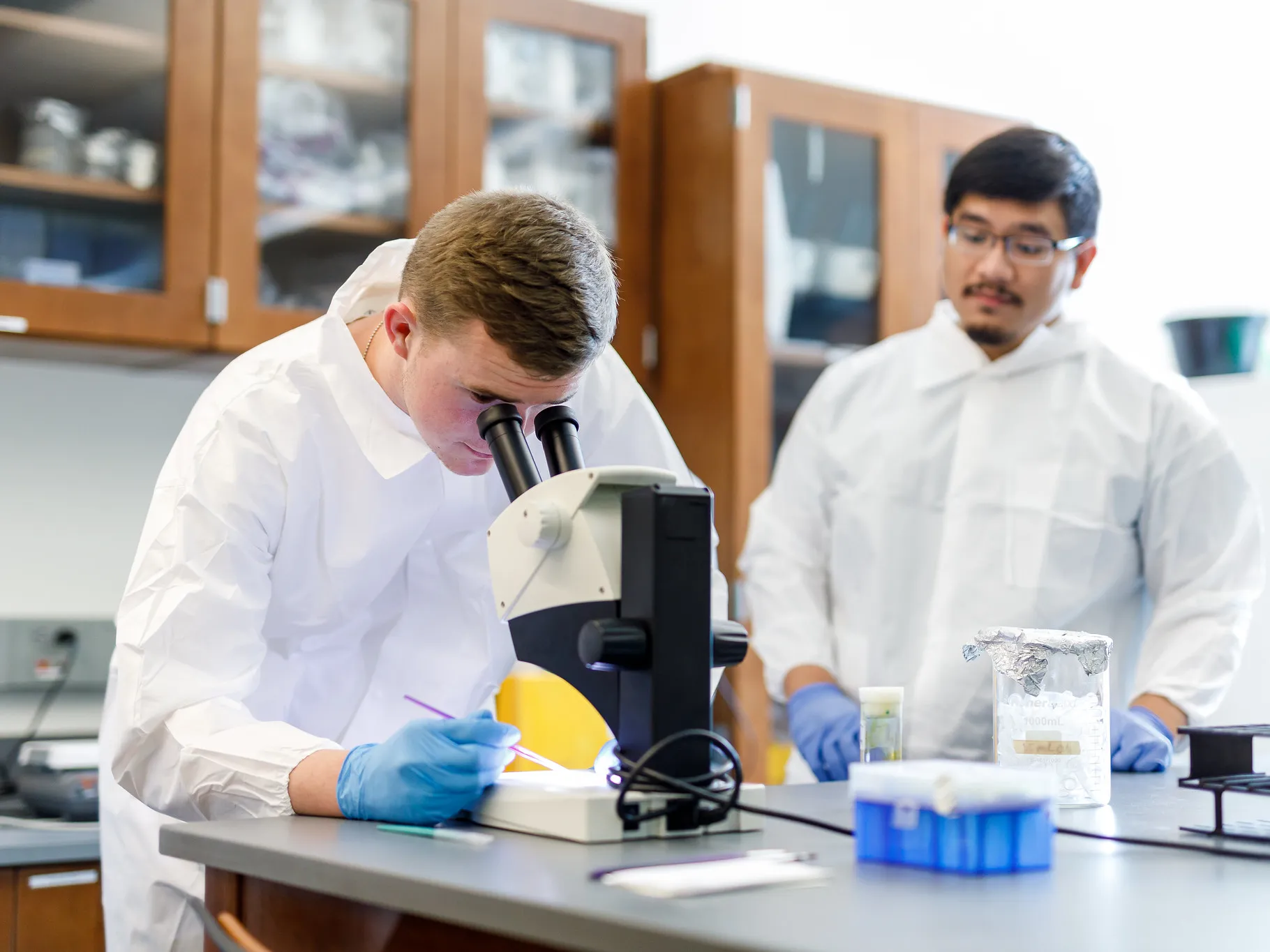 A student looks into a microscope while supervised