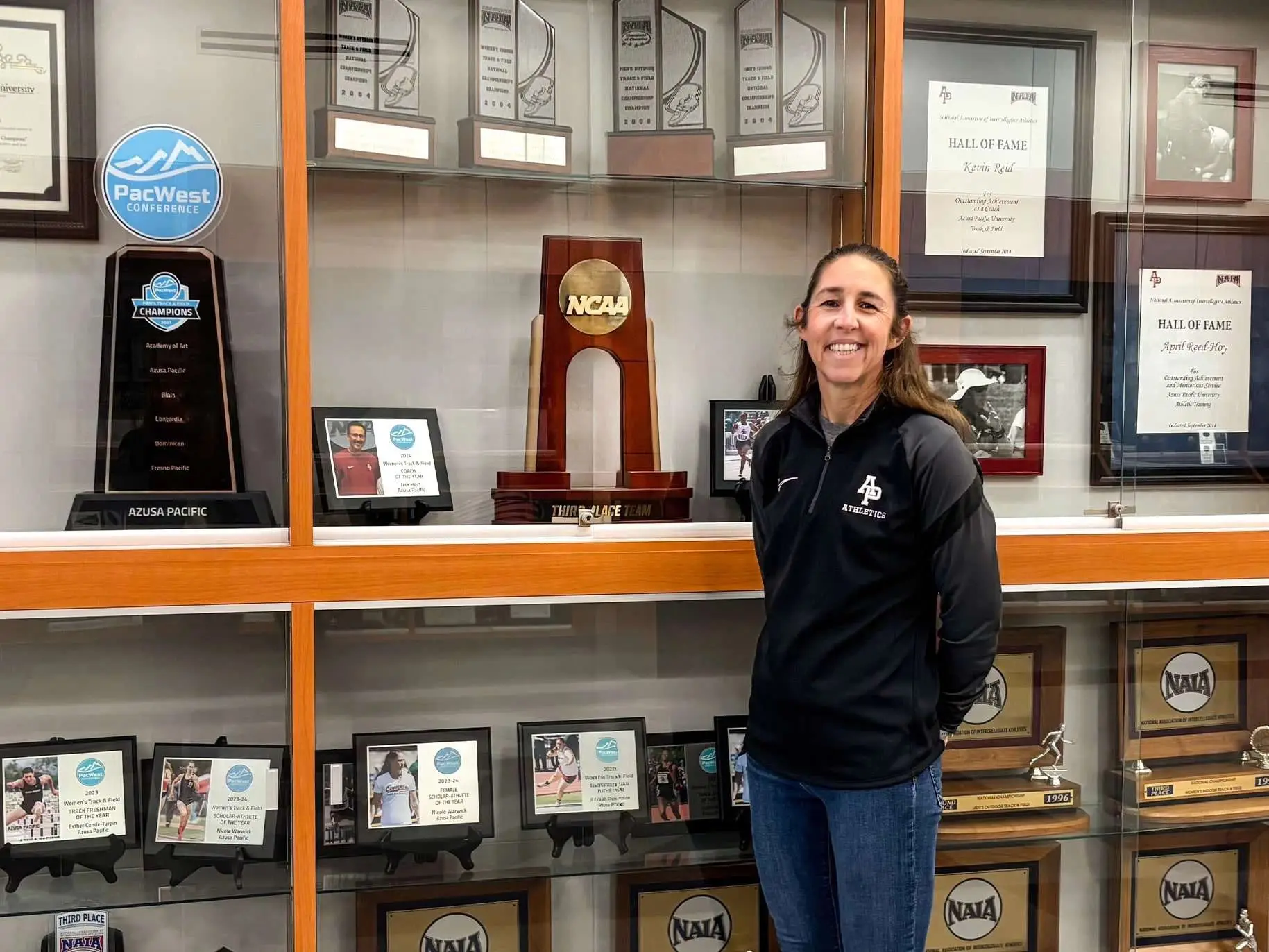 Bethany smiles outside a display of track and field trophies