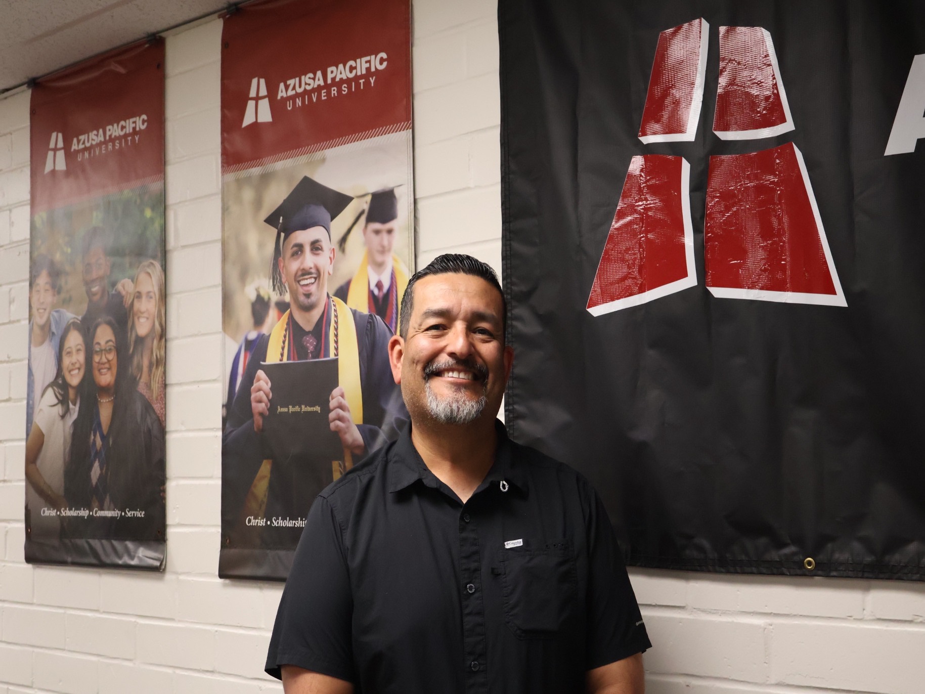 Dante smiles in the information technology office near APU banners