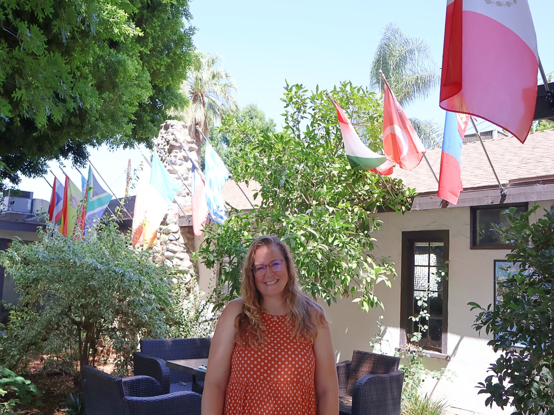 Karen Roughly smiles outside the office of service and discipleship. There are many flags in the background representing different countries.