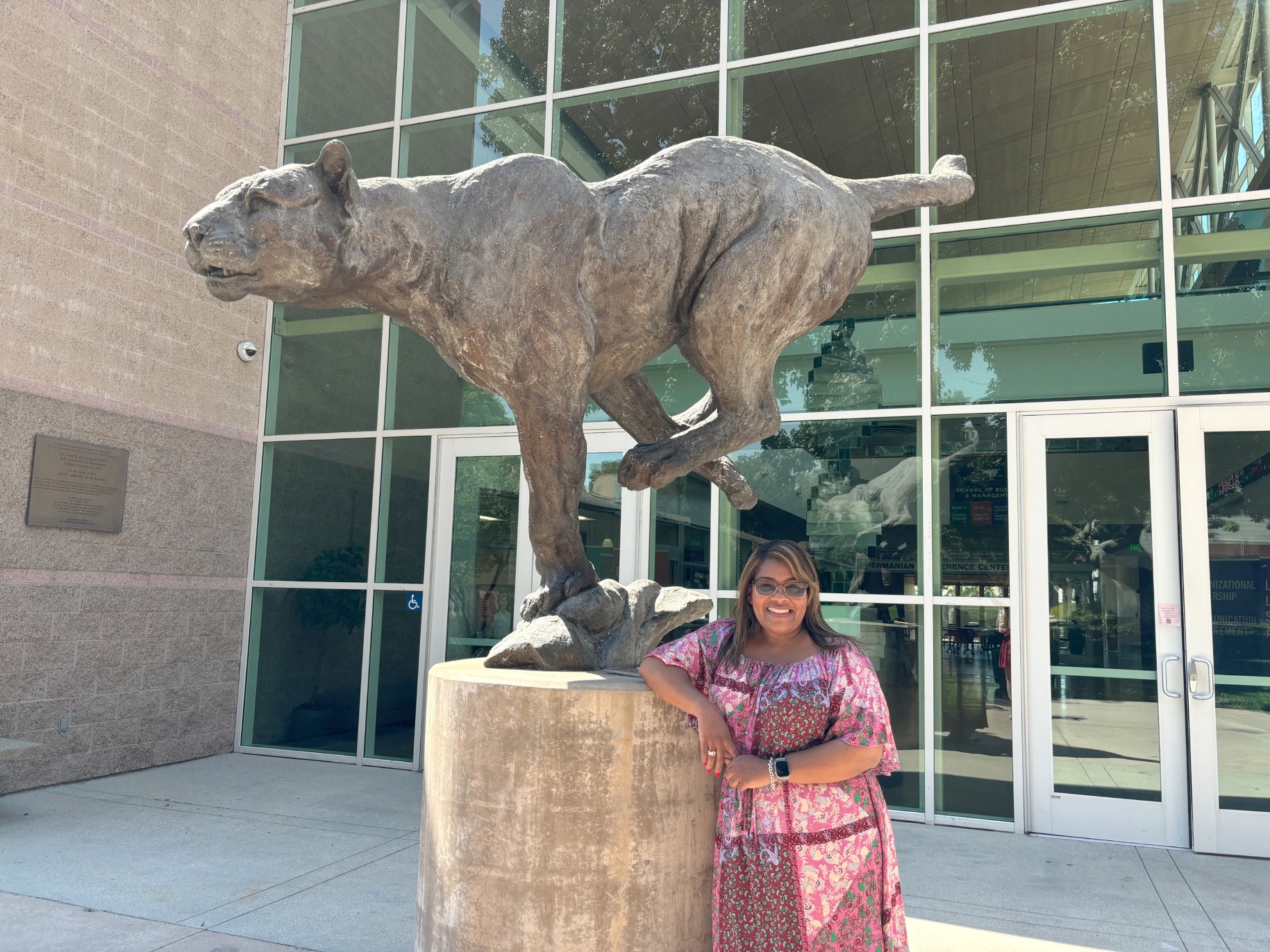 lashan smiles outside the business building, leaning next to a large statue of our mascot, the cougar