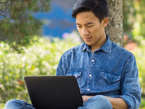 student wearing jeans jacket using his laptop