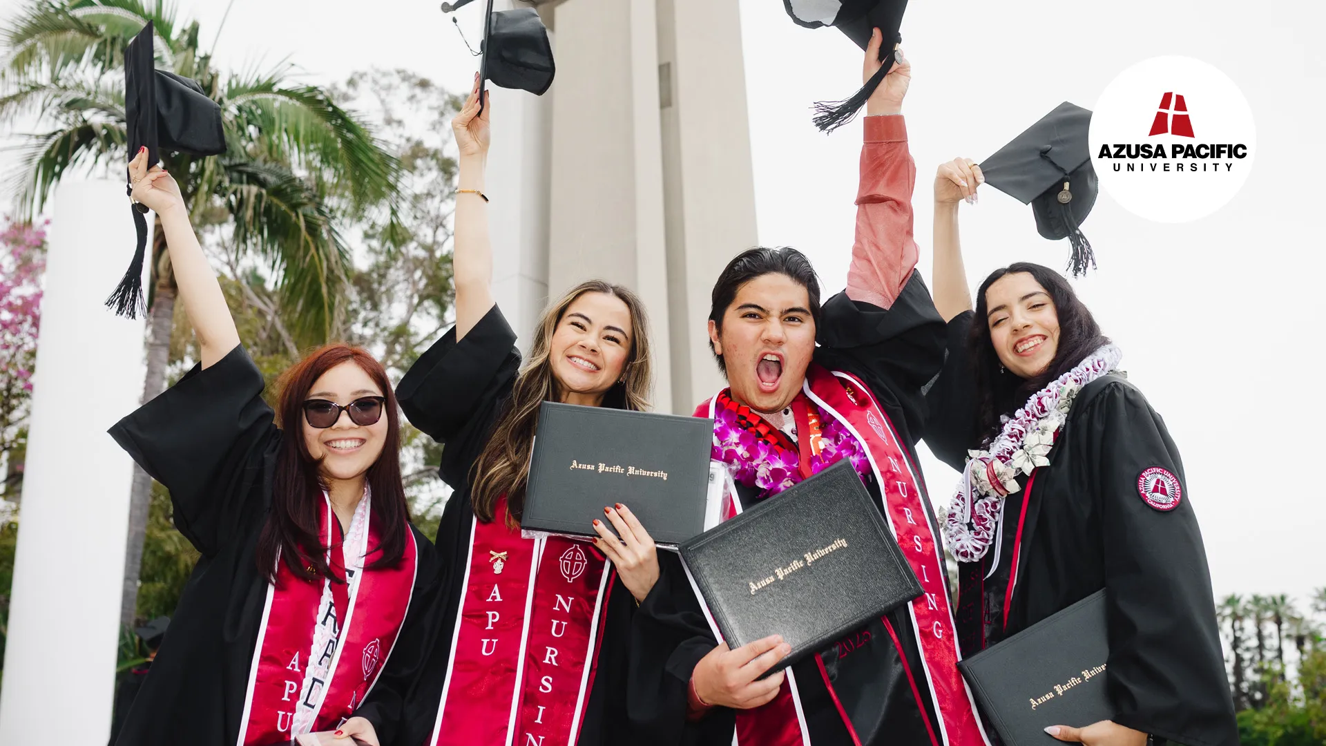 four students wearing black cap and gown holding their diplomas