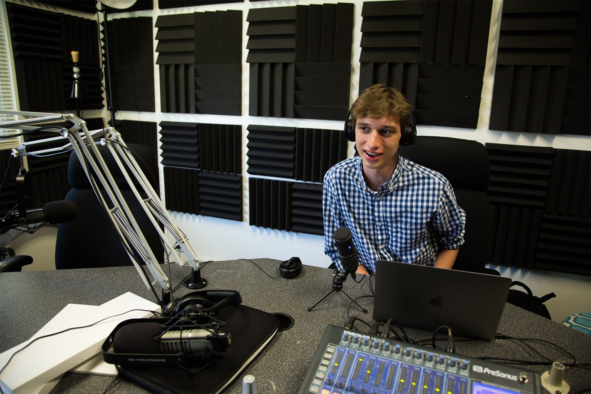 student sitting in a broadcast room speaking into a microphone