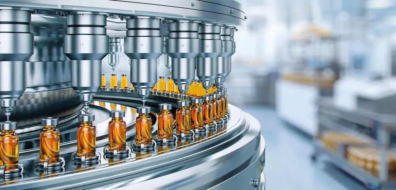 Manufacturing machine with multiple nozzles filling small glass bottles with amber-colored liquid substances.